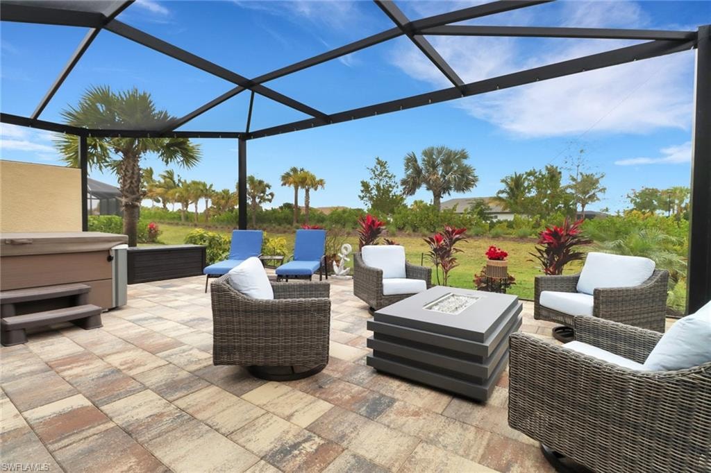 View of patio / terrace featuring a lanai, a hot tub, a sunroom, and an outdoor living space with a fire pit