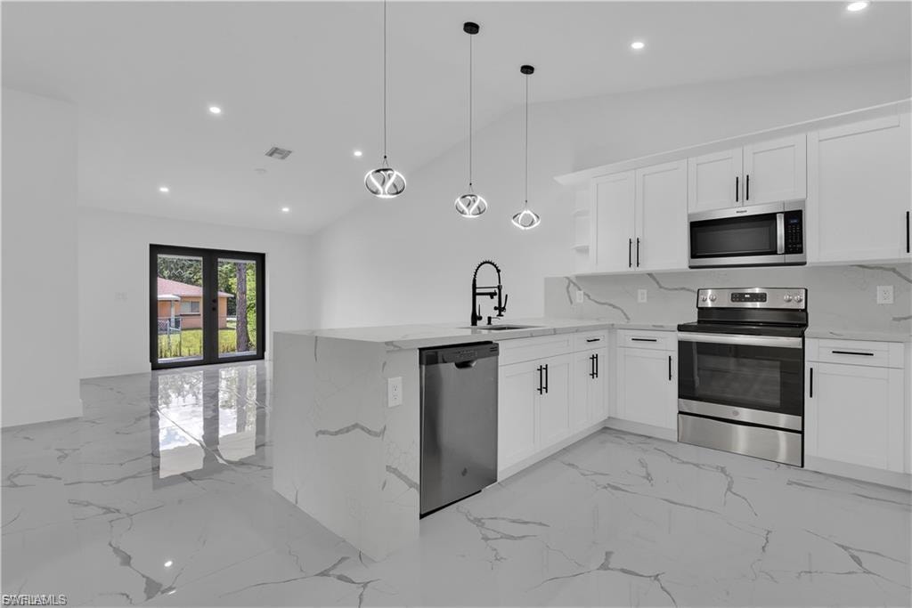 Kitchen featuring stainless steel appliances, a peninsula, white cabinets, light stone countertops, and lofted ceiling