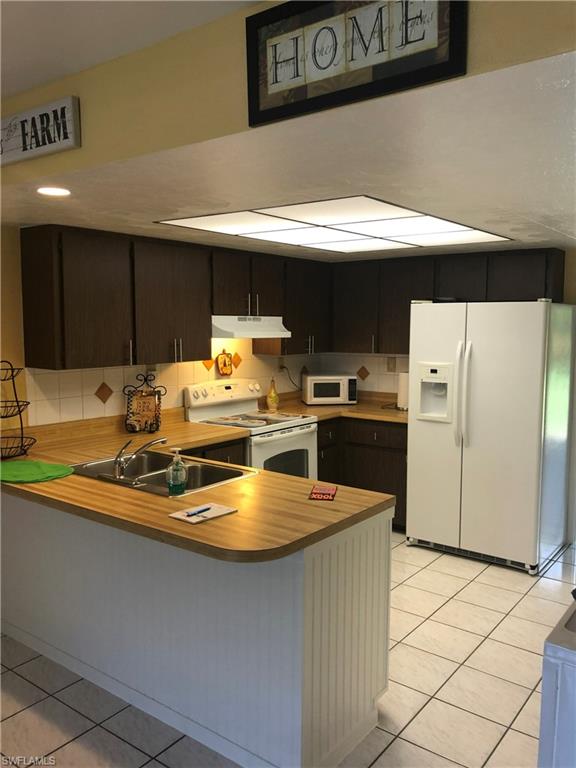 Kitchen with white appliances, light tile patterned floors, a peninsula, and light countertops