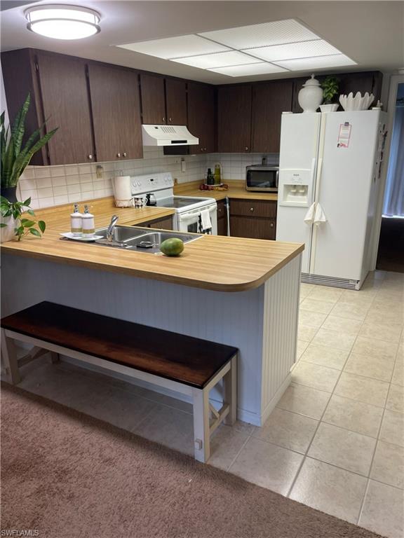 Kitchen featuring white appliances, light countertops, dark wood finish cabinetry, a peninsula, and a kitchen bar