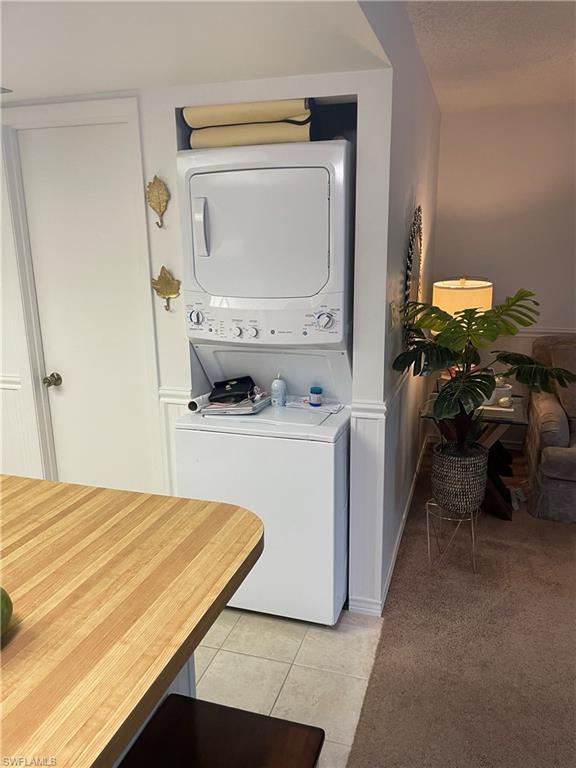Laundry area with stacked washer and dryer, light carpet, light tile patterned floors, a wainscoted wall, and a textured ceiling