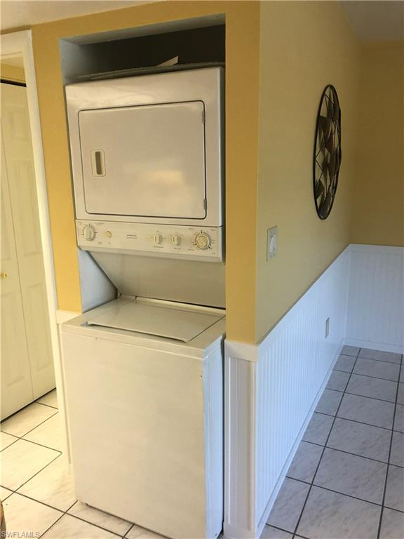 Laundry area featuring wainscoting, stacked washer and dryer, and light tile patterned flooring