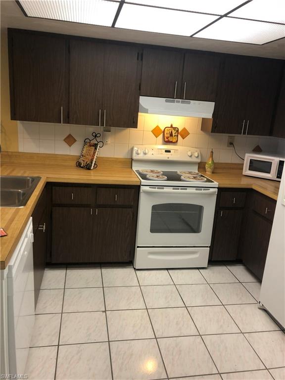 Kitchen with white appliances, light countertops, dark wood finish cabinetry, decorative backsplash, and light tile patterned flooring