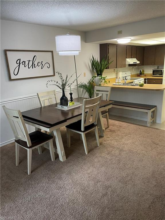 Dining area featuring a textured ceiling, light carpet, and a wainscoted wall