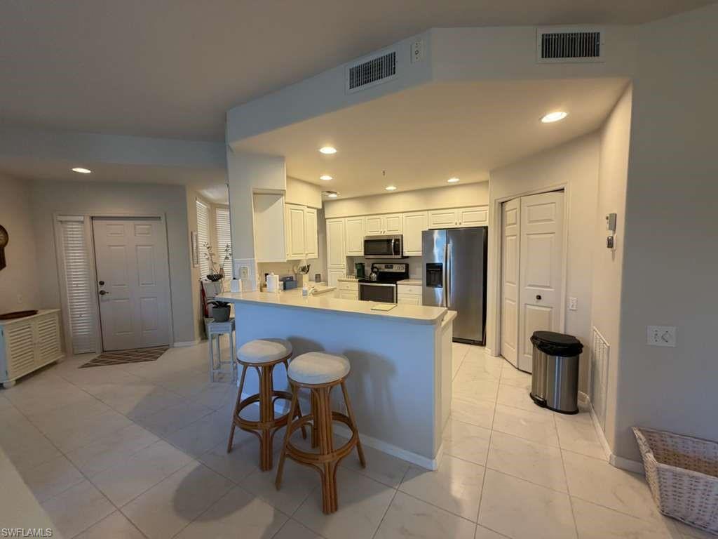 Kitchen featuring a peninsula, white cabinets, stainless steel appliances, a breakfast bar, and light countertops