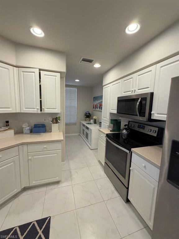 Kitchen with stainless steel appliances, light countertops, white cabinets, and recessed lighting