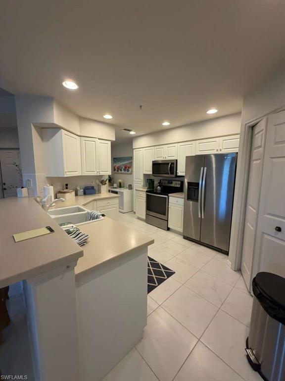 Kitchen featuring stainless steel appliances, light countertops, white cabinetry, a peninsula, and a breakfast bar area