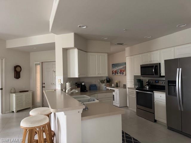 Kitchen featuring stainless steel appliances, a peninsula, light countertops, a kitchen bar, and white cabinets
