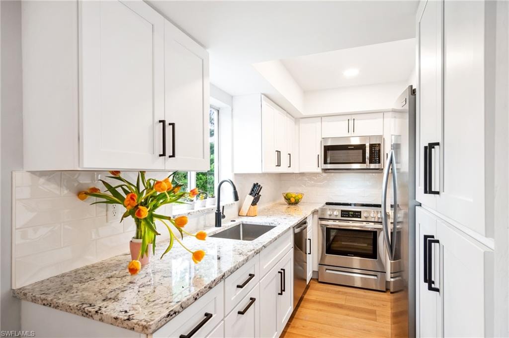 Kitchen with light stone countertops, white cabinets, stainless steel appliances, light wood-style floors, and decorative backsplash