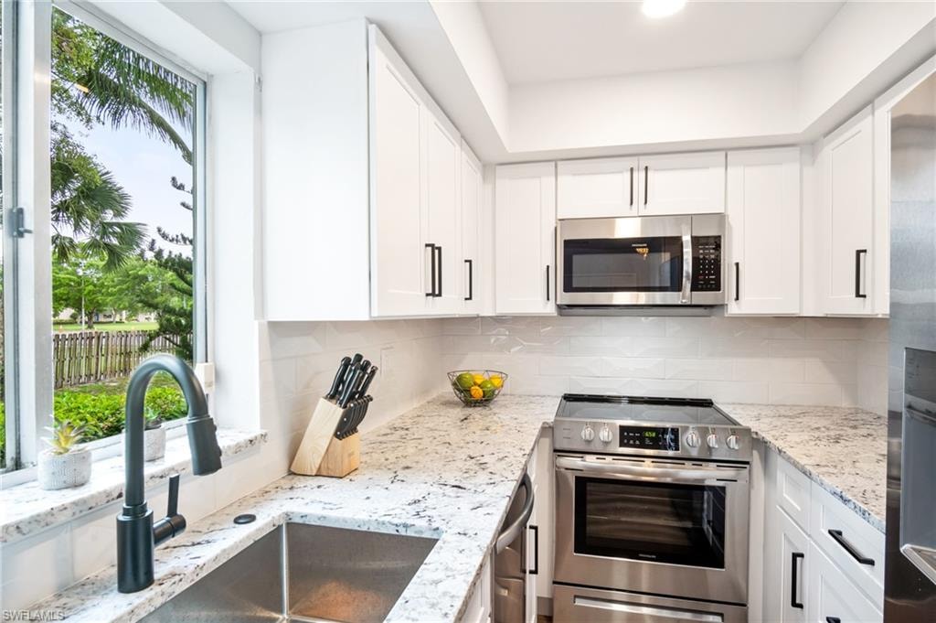 Kitchen featuring stainless steel appliances, white cabinets, and light stone counters
