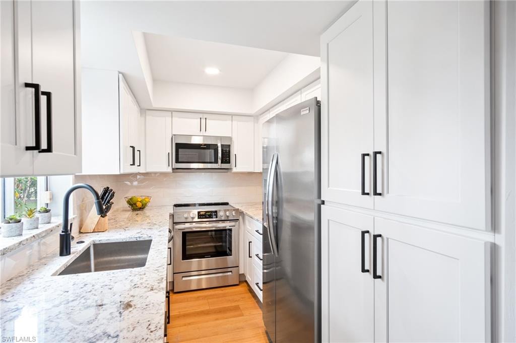 Kitchen featuring stainless steel appliances, light stone countertops, white cabinetry, light wood-style floors, and recessed lighting
