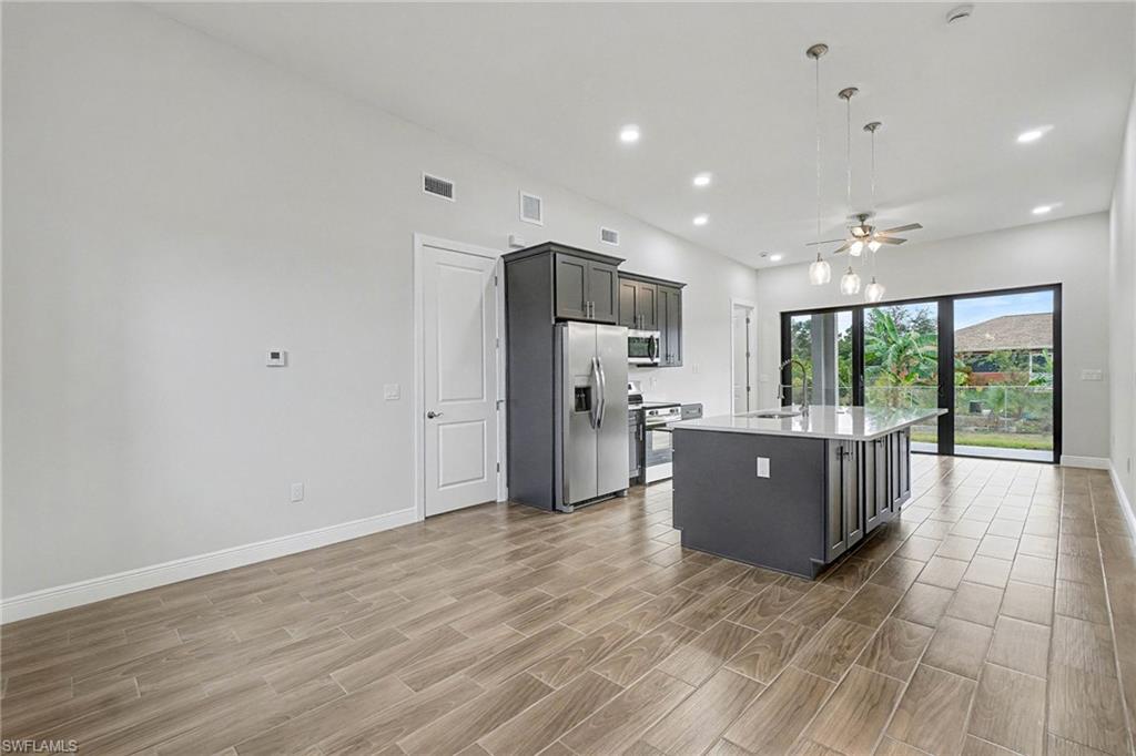 Kitchen featuring hanging light fixtures, an island with sink, wood tiled floors, a ceiling fan, and stainless steel appliances