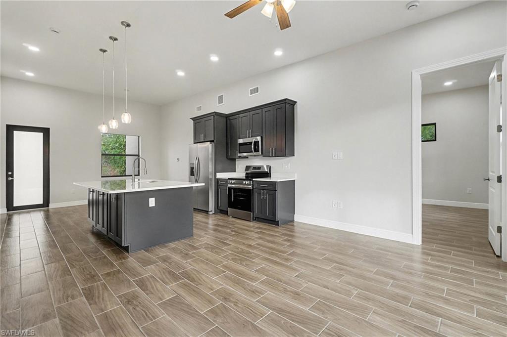 Kitchen featuring stainless steel appliances, a kitchen island with sink, ceiling fan, wood finish floors, and decorative light fixtures