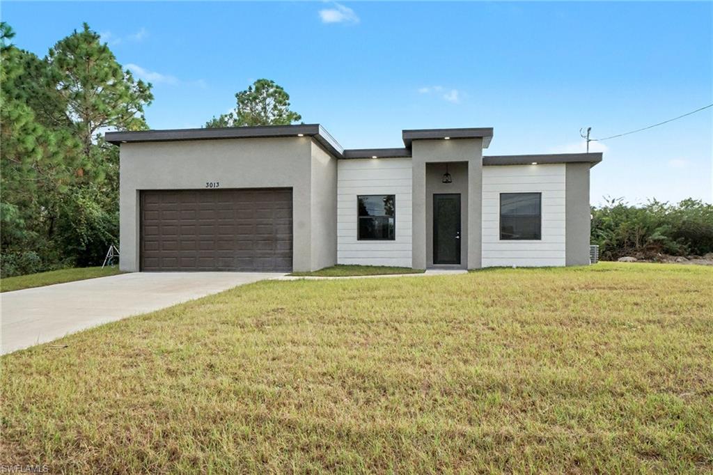 Modern home with a front yard, concrete driveway, a garage, and stucco siding