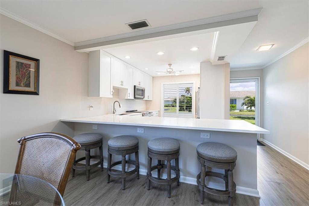 Kitchen with a expansive peninsula, a kitchen breakfast bar, crown molding, light wood-style floors, and white cabinets