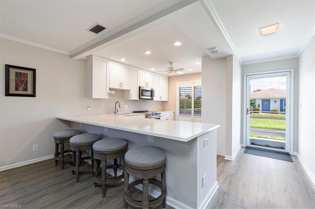 Kitchen featuring light wood-style flooring, a peninsula, a breakfast bar, crown molding, and white cabinetry