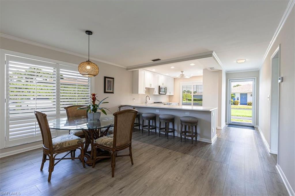 Dining area featuring crown molding, light wood-style flooring, ceiling fan and expansive kitchen peninsula and breakfast bar