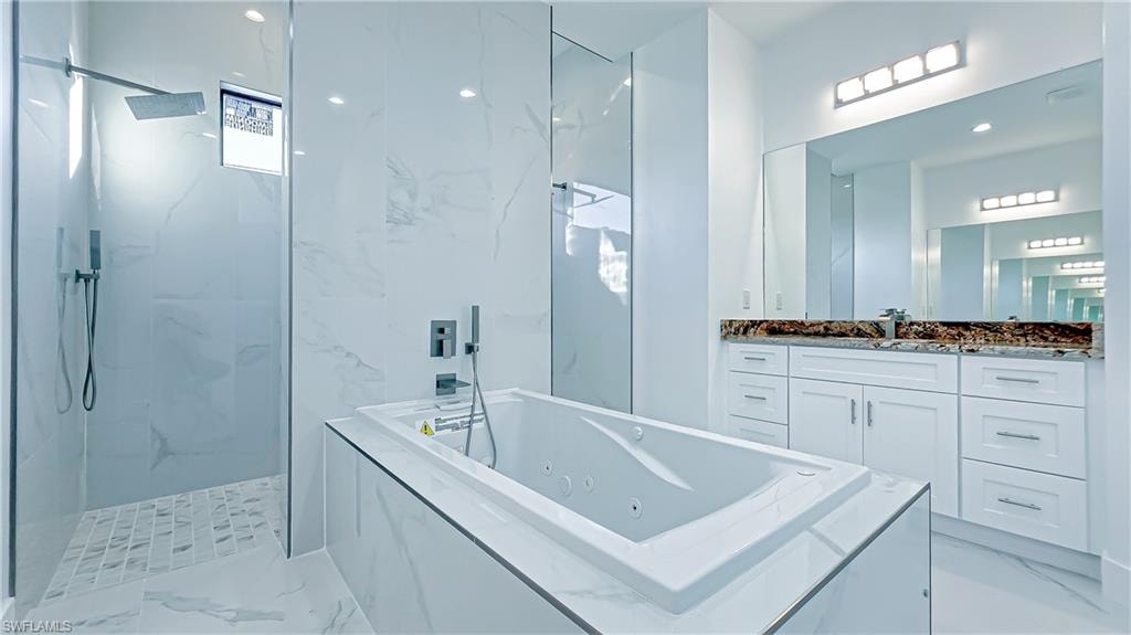 Bathroom with a marble finish shower, vanity, and a jetted tub