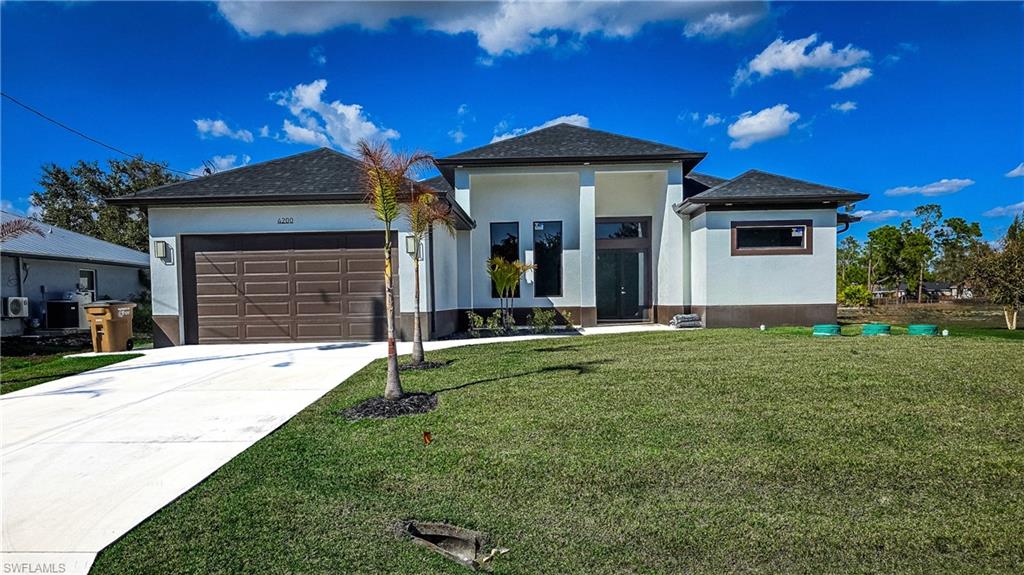 View of front of property featuring a garage, stucco siding, driveway, and a front yard