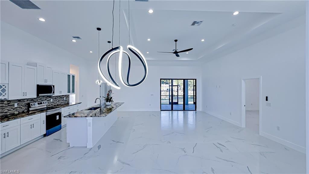 Kitchen with stainless steel appliances, white cabinetry, dark stone countertops, a center island with sink, and open floor plan