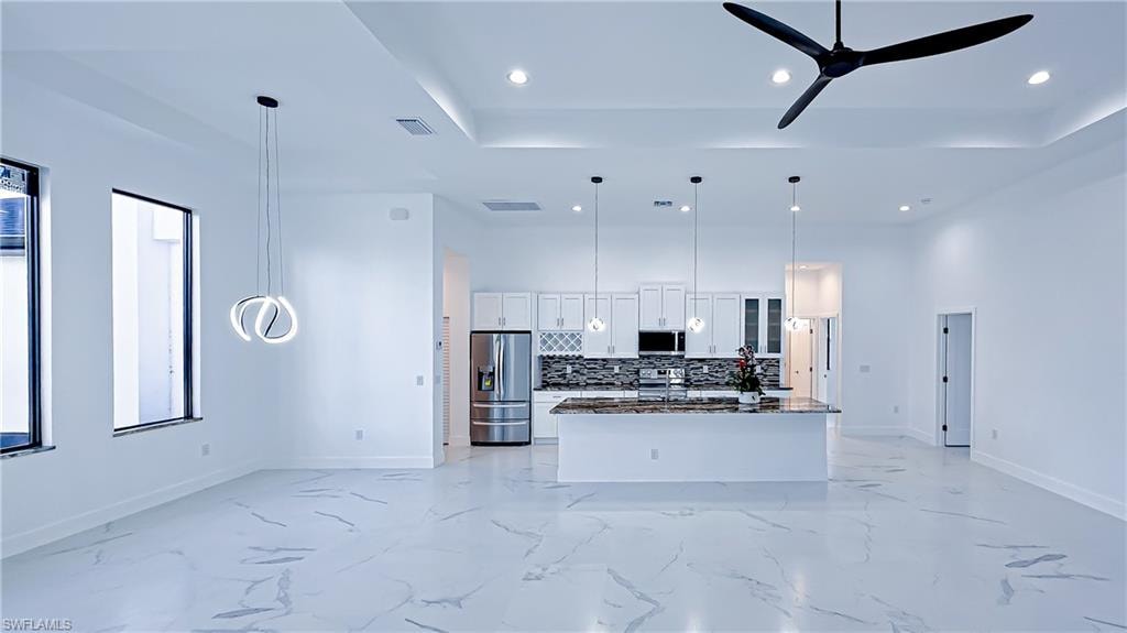 Kitchen with white cabinetry, open floor plan, stainless steel appliances, pendant lighting, and dark stone counters
