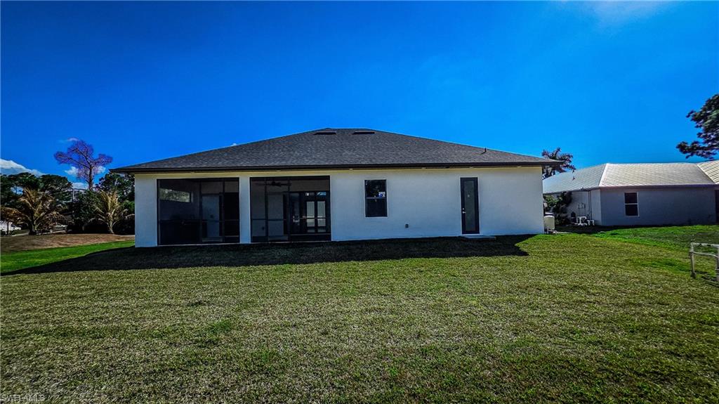 Back of property with a lawn, stucco siding, and a sunroom