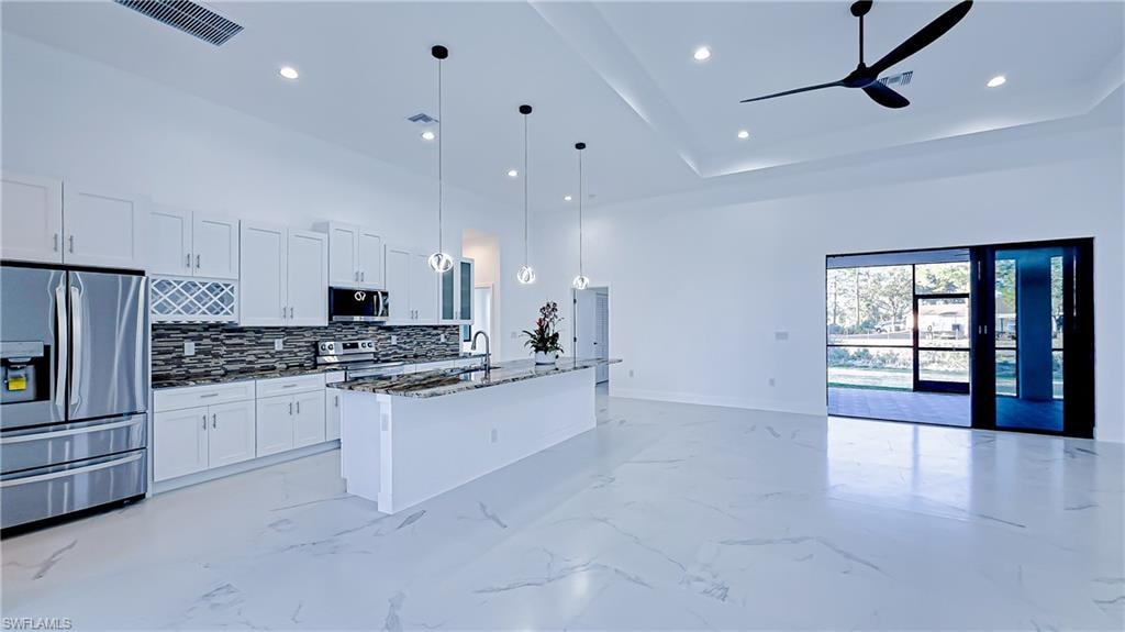 Kitchen featuring stainless steel appliances, open floor plan, white cabinetry, pendant lighting, and a center island with sink