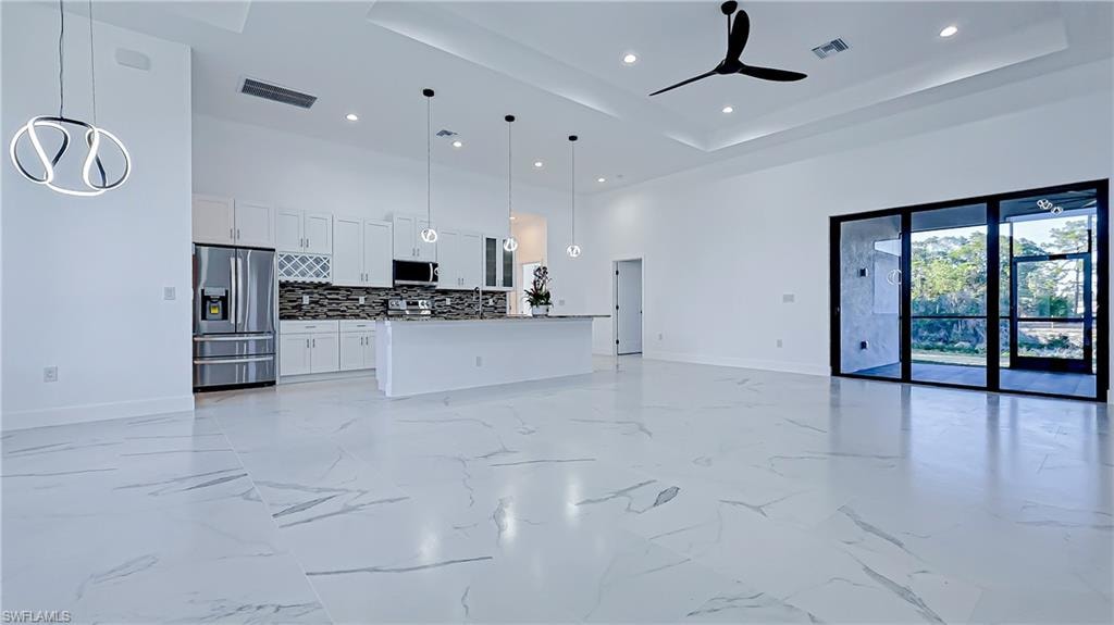 Unfurnished living room with a high tray ceiling, recessed lighting, and ceiling fan