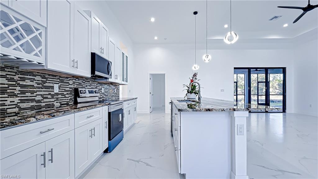 Kitchen featuring stainless steel appliances, dark stone countertops, white cabinetry, pendant lighting, and an island with sink