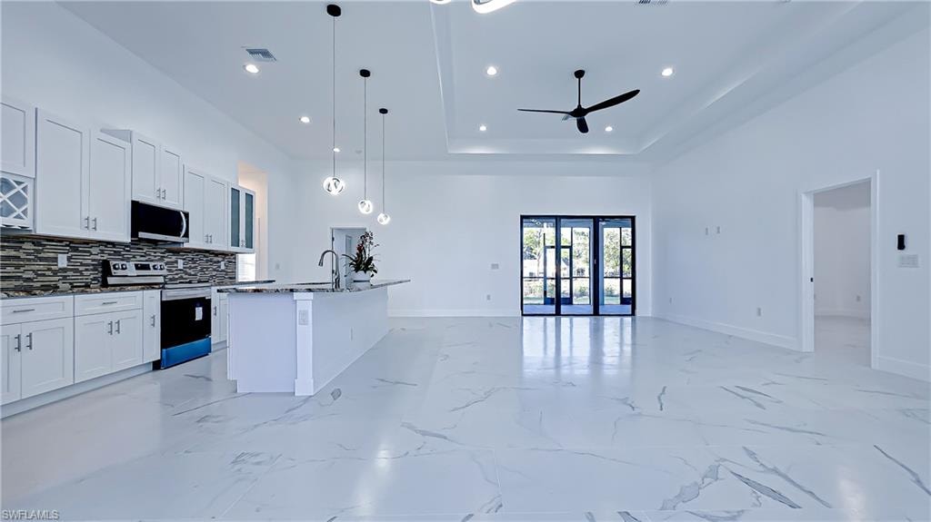 Kitchen featuring stainless steel appliances, white cabinets, open floor plan, hanging light fixtures, and a tray ceiling