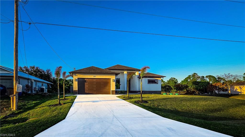 Prairie-style home featuring a front lawn, concrete driveway, stucco siding, and a garage