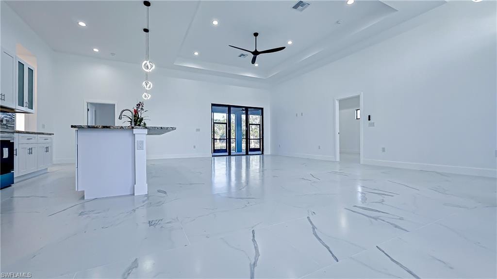Kitchen featuring white cabinets, pendant lighting, an island with sink, open floor plan, and dark stone countertops