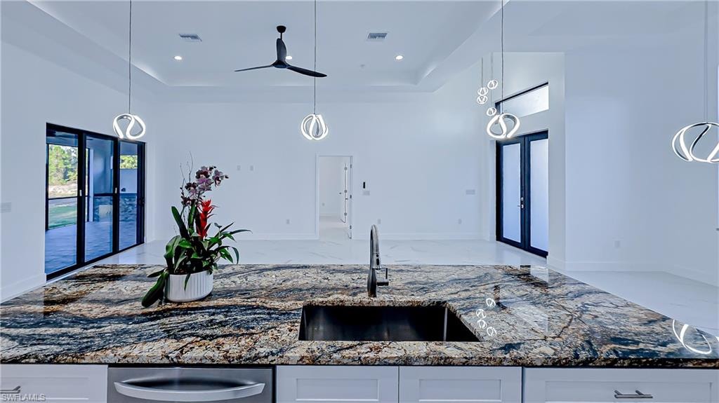 Kitchen featuring dark stone countertops, decorative light fixtures, white cabinetry, and a raised ceiling