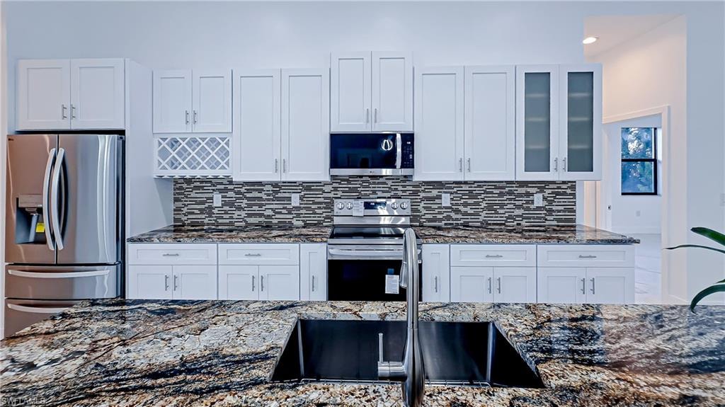 Kitchen featuring dark stone countertops, stainless steel appliances, white cabinetry, glass insert cabinets, and recessed lighting