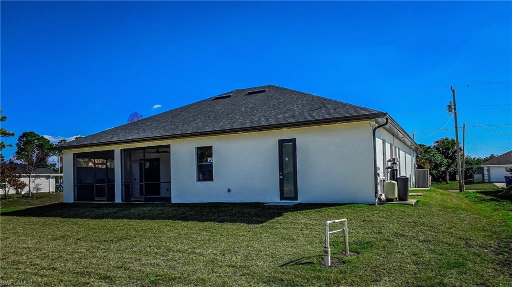 Rear view of house featuring a yard, stucco siding, roof with shingles, and a sunroom