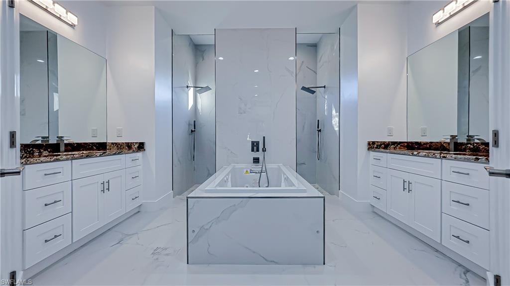 Bathroom with a marble finish shower, a garden tub, two vanities, and stone wall