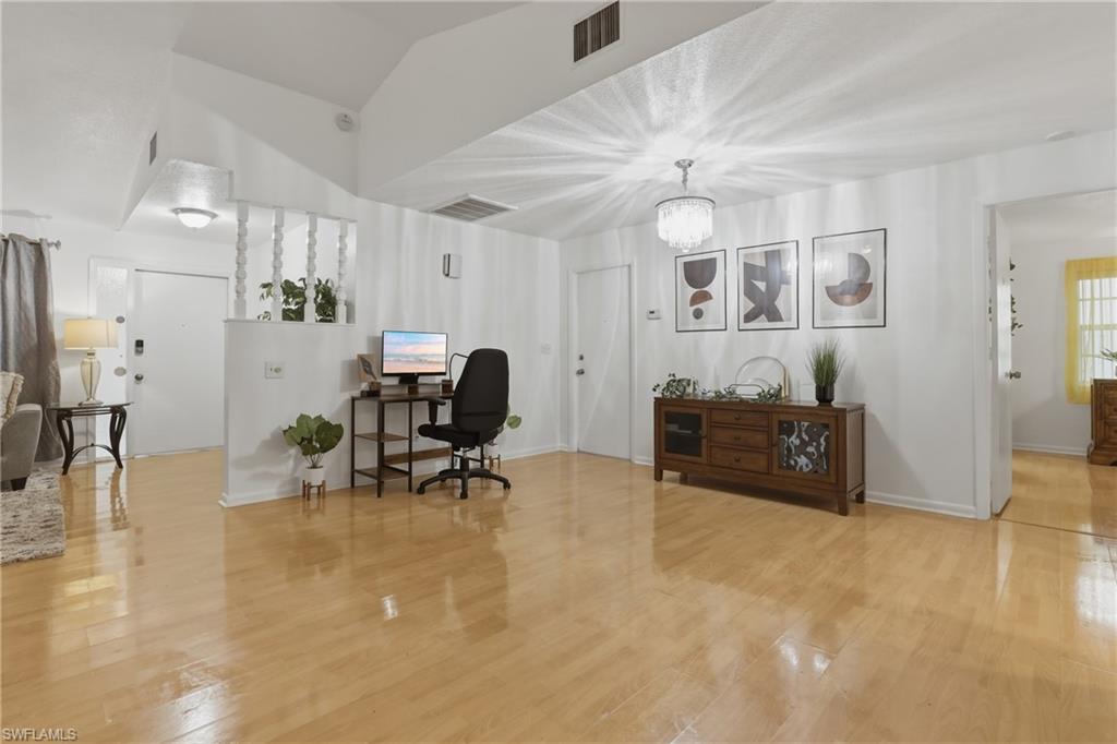 Office space with vaulted ceiling, suspended lighting, and light wood-style floors