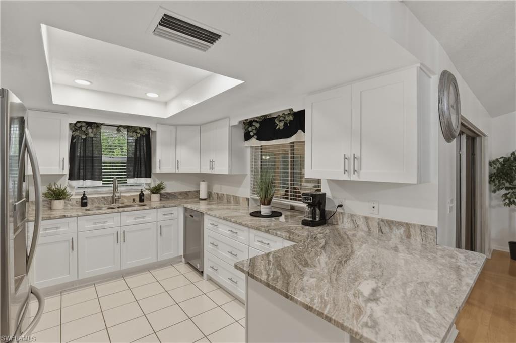 Kitchen with white cabinets, light stone counters, stainless steel appliances, a tray ceiling, and a peninsula