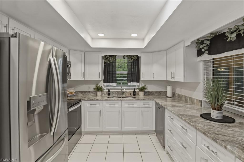 Kitchen featuring stainless steel appliances, white cabinets, a raised ceiling, recessed lighting, and light stone counters