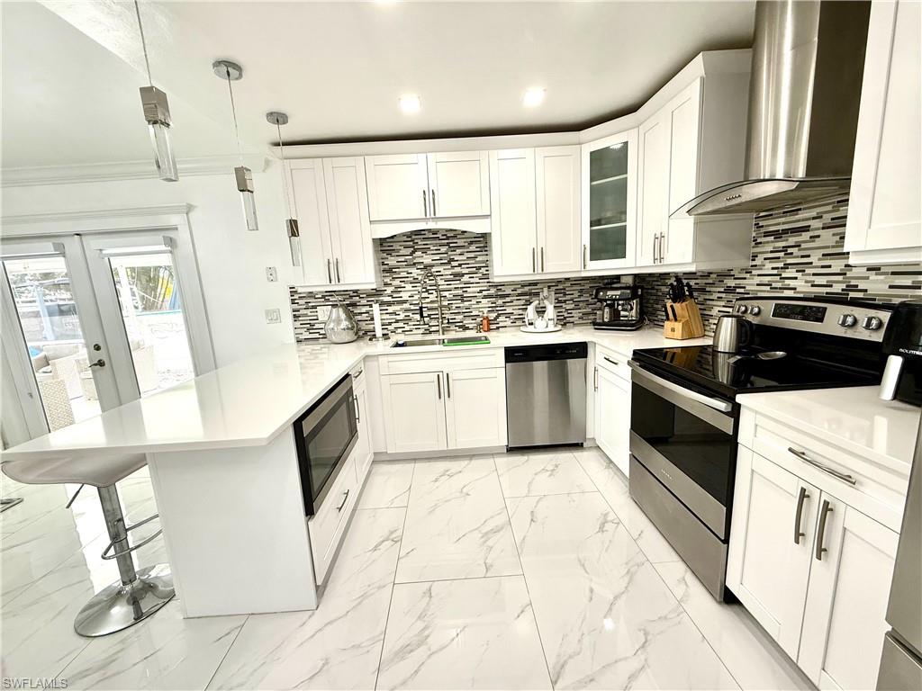 Kitchen featuring stainless steel appliances, pendant lighting, white cabinets, light marble finish flooring, and glass fronted cabinets