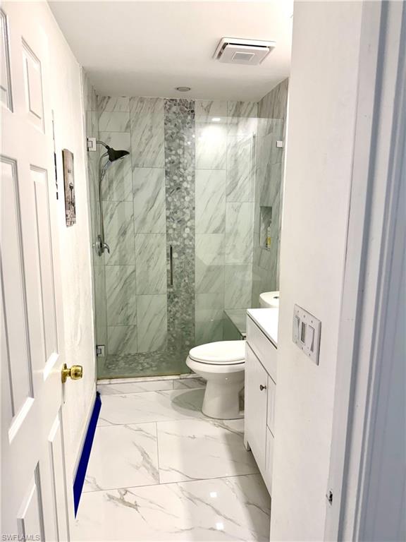 Bathroom featuring vanity, a marble finish shower, and light marble finish floors