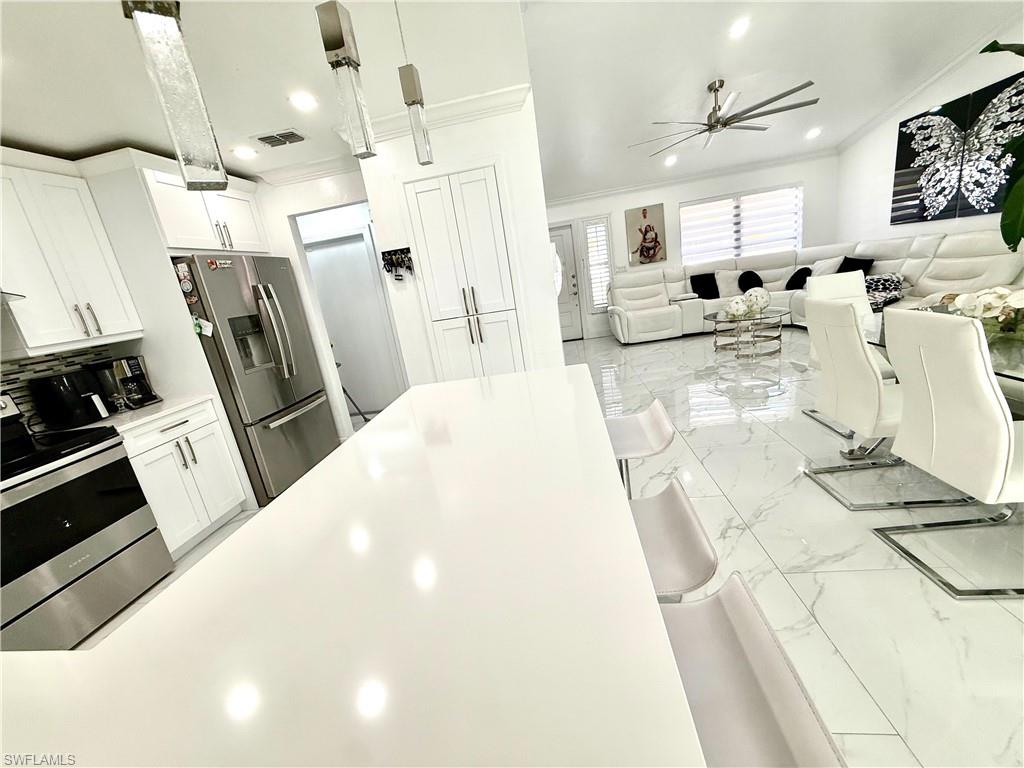 Kitchen featuring ornamental molding, white cabinets, stainless steel appliances, pendant lighting, and light marble finish flooring