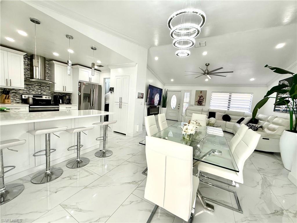 Dining room featuring crown molding, light marble finish flooring, hanging lights, a ceiling fan, and lofted ceiling