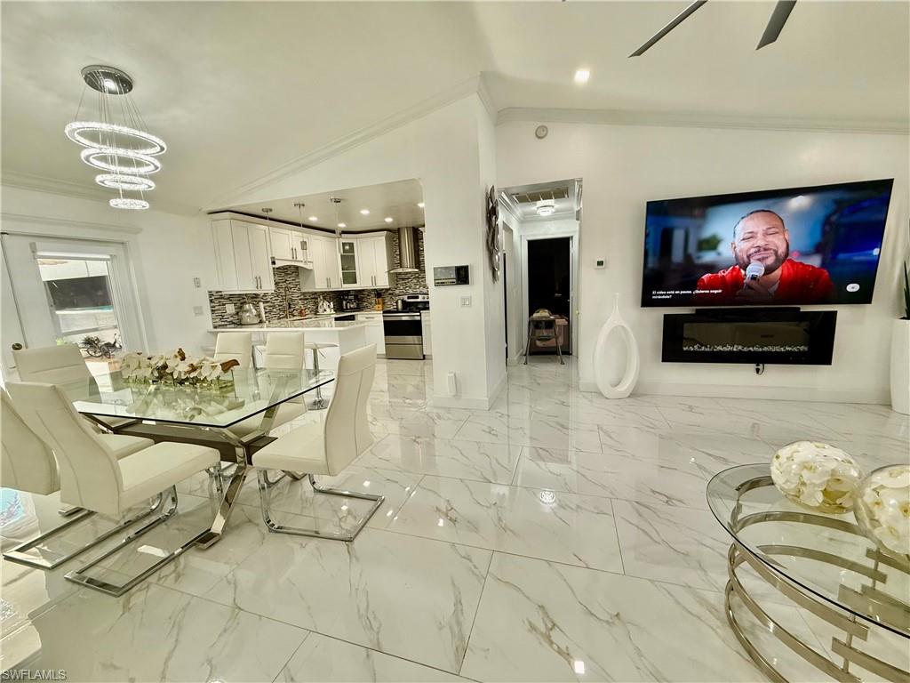Dining room with suspended lighting, lofted ceiling, ornamental molding, ceiling fan, and light marble finish flooring