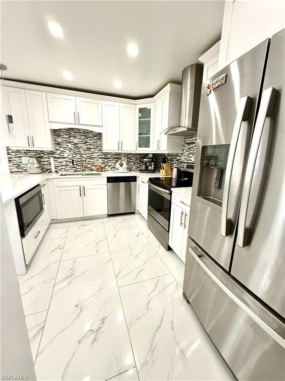 Kitchen with light marble finish flooring, stainless steel appliances, white cabinets, glass insert cabinets, and recessed lighting