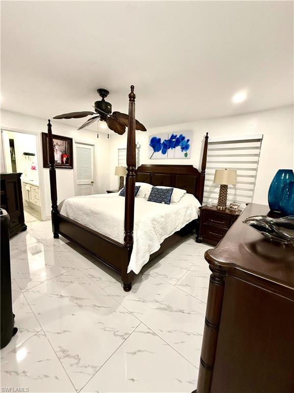 Bedroom with ensuite bath, a ceiling fan, and light marble finish flooring