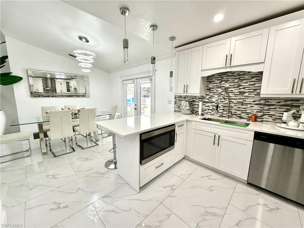 Kitchen with white cabinets, stainless steel appliances, a peninsula, ornamental molding, and light marble finish floors