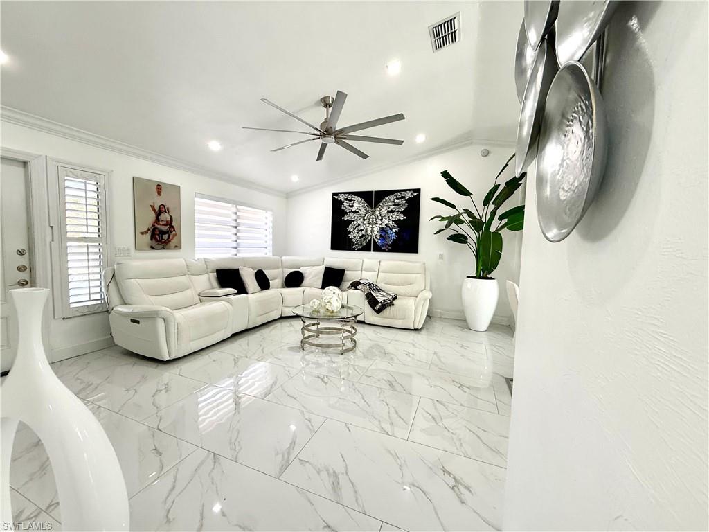 Living area featuring lofted ceiling, crown molding, recessed lighting, light marble finish floors, and ceiling fan