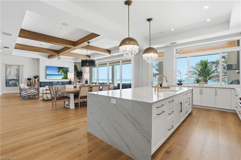 Kitchen featuring light stone countertops, light wood-style floors, a large island, open floor plan, and coffered ceiling - Virtually Edited Image