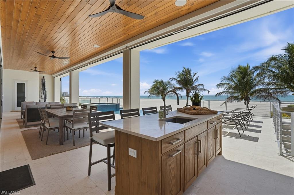 View of patio with ceiling fan, a water view, an outdoor bar and dining area, and exterior kitchen - Virtually Edited Image